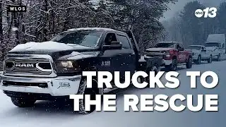 3 trucks pull a tractor-trailer up a snow-covered mountain road
